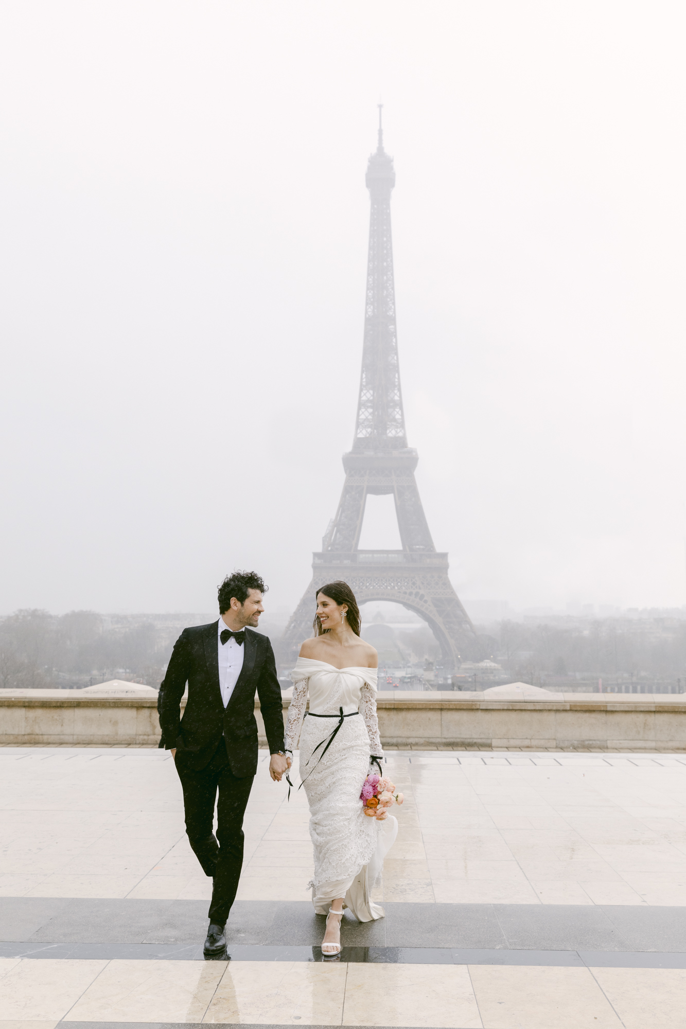 Bride and groom at Trocadéro in Paris, France. Walking away from the Eiffel Tower on a rainy day in their wedding dress and tuxedo.