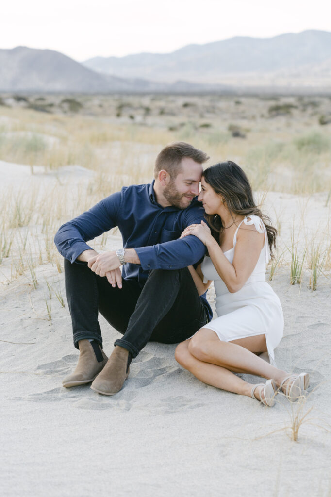 couple sitting in sand during their engagement session