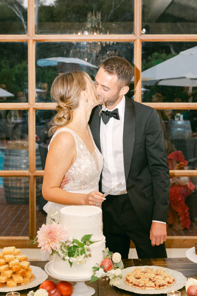 newlyweds kissing after cutting their wedding cake 