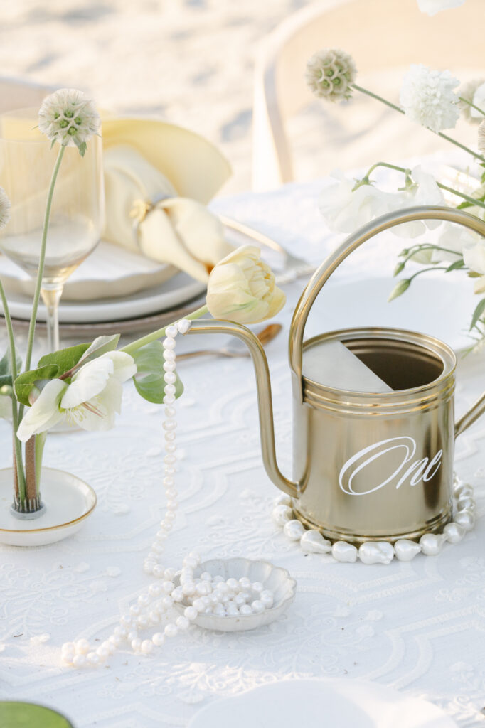 a gold water pitcher with number "one" dripped with pearls used as a table number for a destination wedding in San Diego