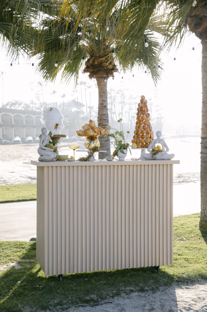 Dessert and cake bar with custom beehive design cake, croissant bouquet, and pastry tower, for beach destination wedding in San Diego.