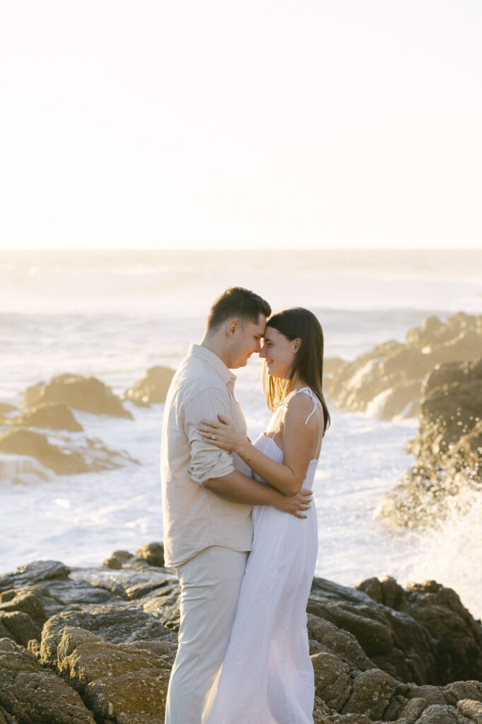 couple embracing on rocky Pebble Beach shoreline during sunset engagement session in California