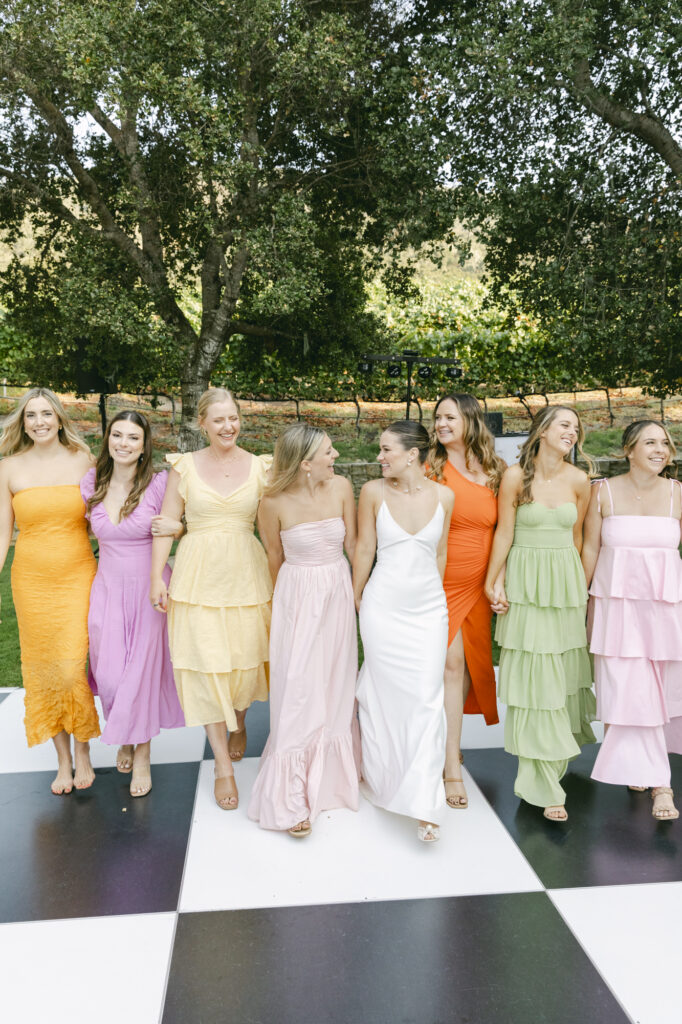 bride and her bridesmaids walking across checkered dance floor during wedding reception.