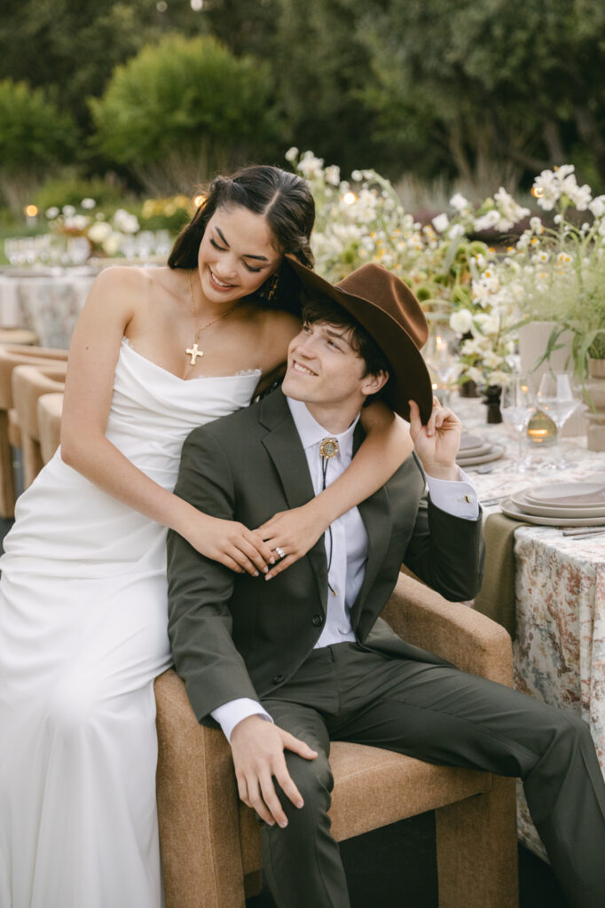Bride and groom in western wedding attire sharing an intimate moment at reception table with floral details at Holman Ranch in Carmel Valley, California, captured in editorial style wedding photography.