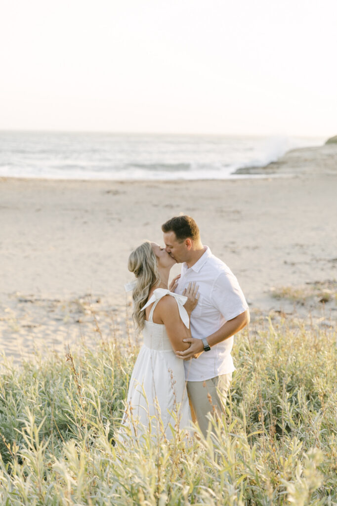 couple kissing in coastal grass during golden hour engagement session at Natural Bridges State Beach in Santa Cruz