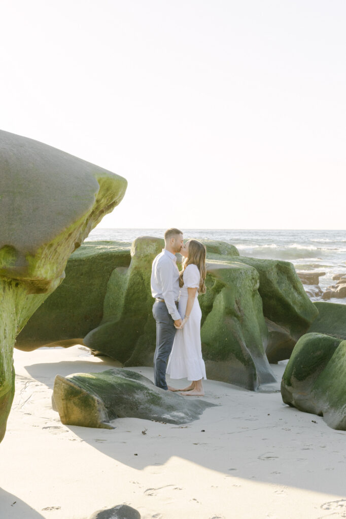 couple kissing between iconic rock formations at Windnsea Beach during a romantic San Diego engagement session