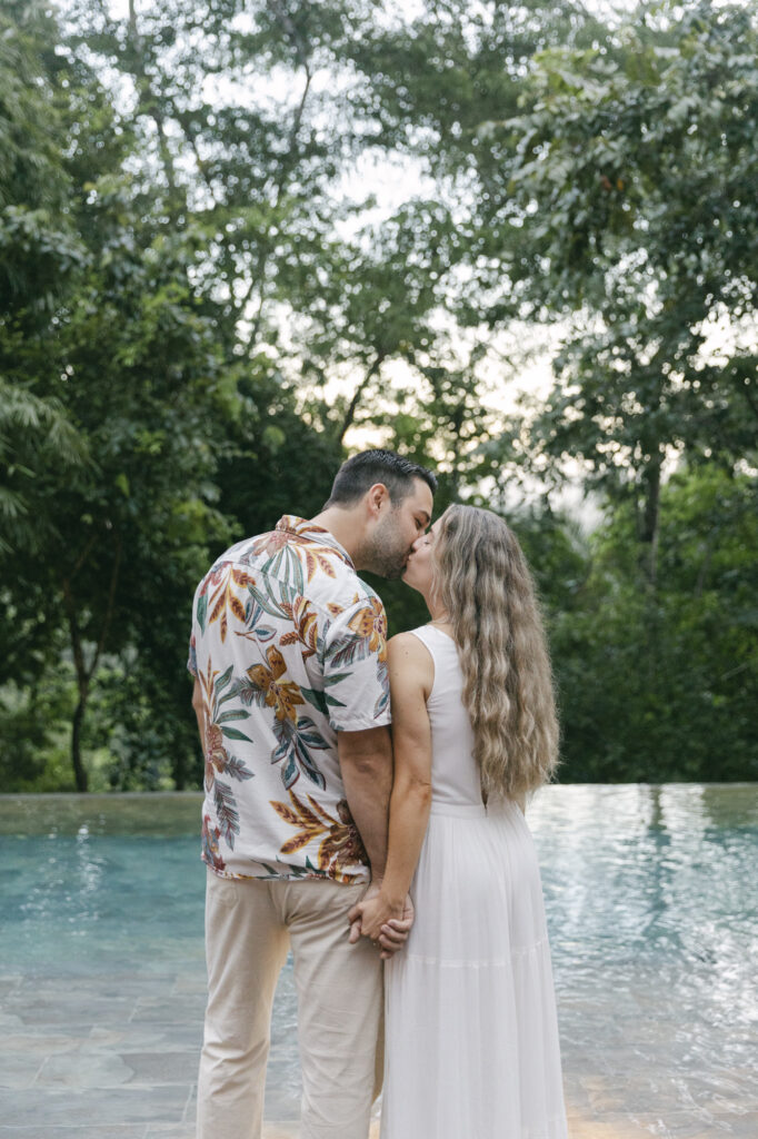 Couple kissing beside a jungle infinity pool surrounded by rainforest, Belize destination wedding photographer Paulina Perrucci