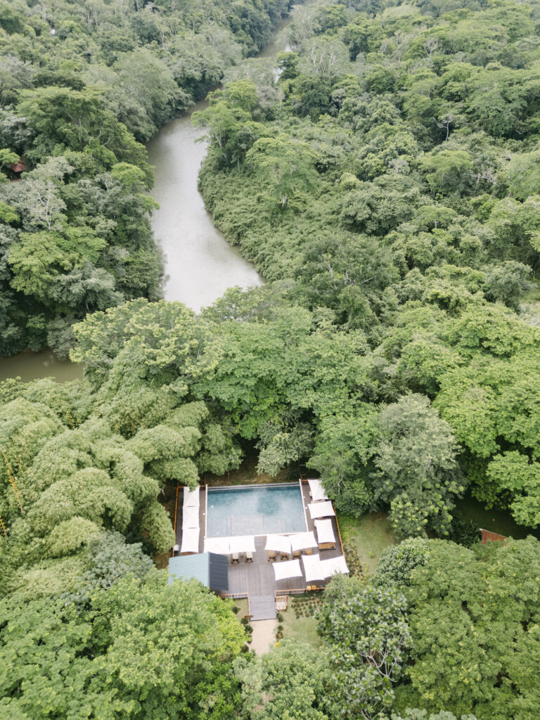 Aerial view of a rainforest resort pool tucked along a winding jungle river, Belize destination wedding photographer Paulina Perrucci