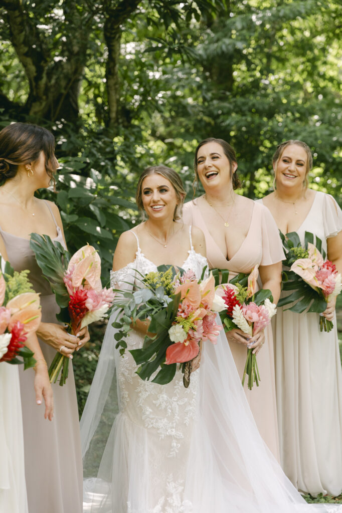 Bride laughing with her bridesmaids holding tropical monstera and anthurium bouquets in the rainforest, Belize destination wedding photographer Paulina Perrucci