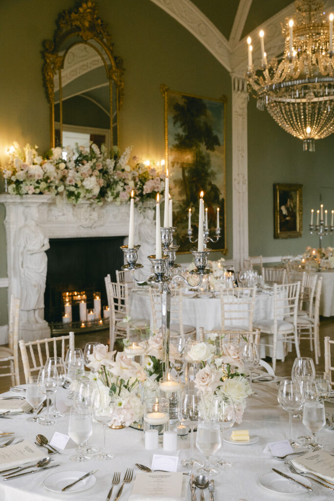 Romantic Luttrellstown Castle wedding reception featuring a floral mantle, candlelit fireplace, and crystal chandelier.