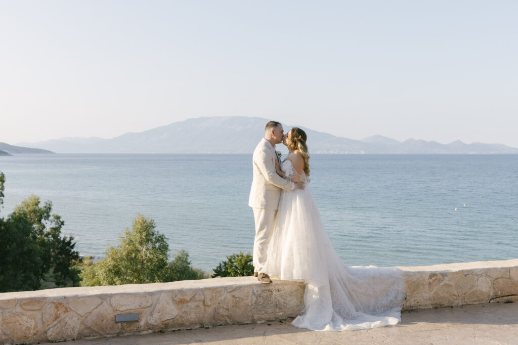 Bride and groom kissing with panoramic ocean and mountain views during a luxury Zakynthos Greece destination wedding with editorial style wedding photography.
