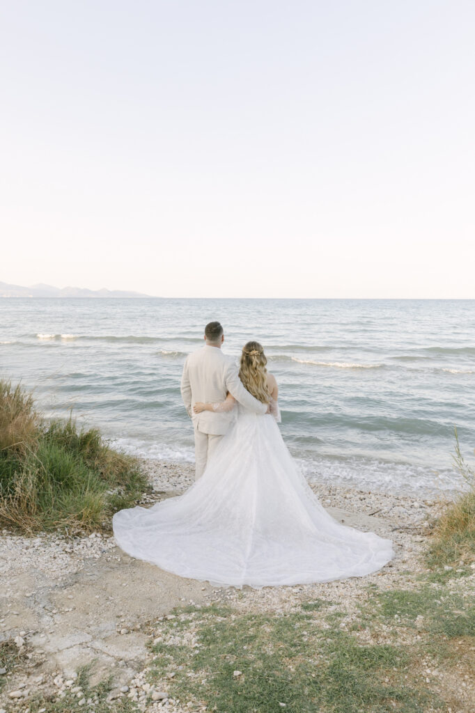 Bride and groom holding hands on a rocky beach during a luxury Zakynthos destination wedding with romantic ocean views and editorial style wedding photography.