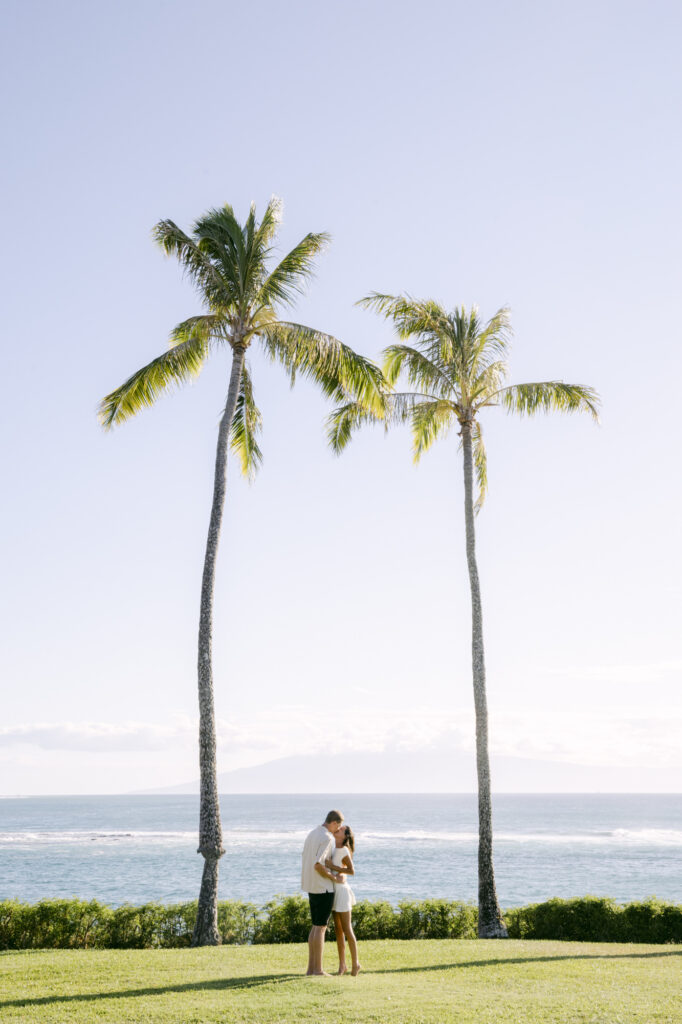 Couple embracing between two tall palm trees during a Maui Hawaii engagement session with the Pacific Ocean and blue sky in the background