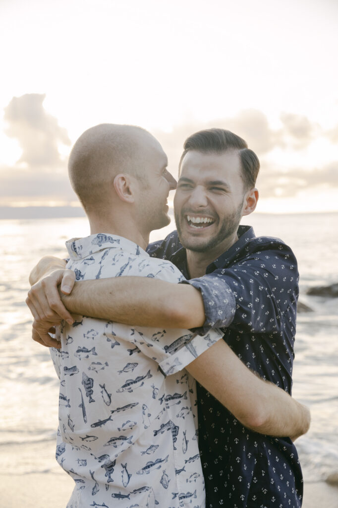LGBTQ gay couple laughing and embracing during their Maui engagement session on the beach at golden hour