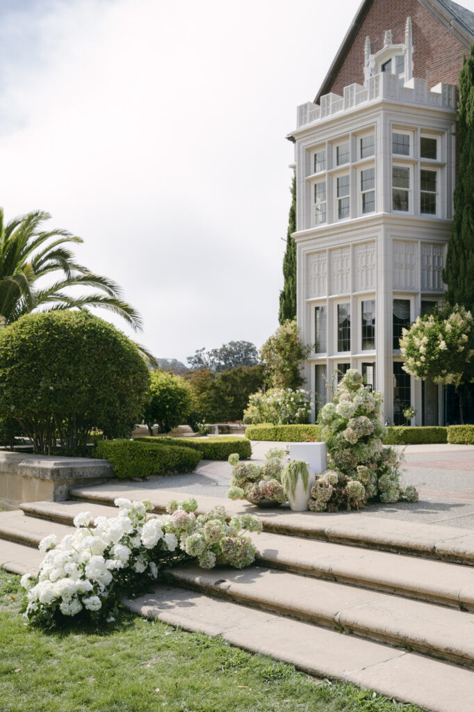 White hydrangea floral installation cascading down the stone entry steps at Kohl Mansion with the Gothic Tudor facade in the background for a luxurious wedding.