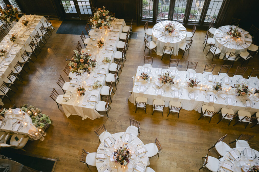 Aerial view of the Kohl Mansion Great Hall reception with long farm tables, round tables, chiavari chairs, and peach and blush floral centerpieces