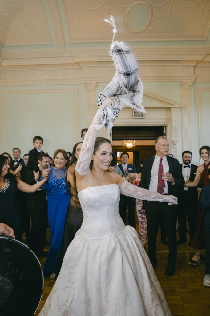 Bride in a strapless ballgown with lace gloves raising her arms in celebration during the zaffa procession at her Kohl Mansion wedding reception