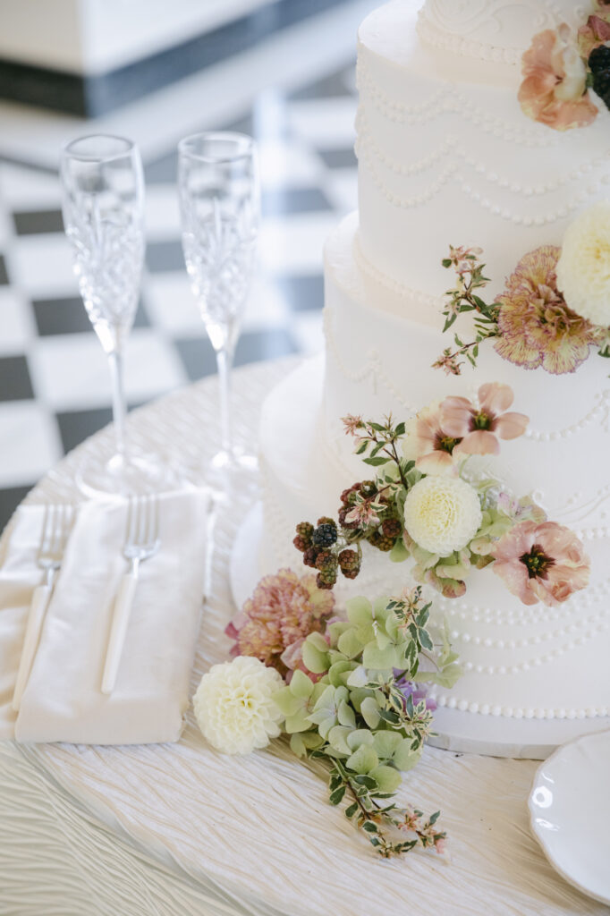 Wedding cake with cascading blush and white fresh flowers and crystal champagne flutes on the black and white marble floor at Kohl Mansion in Burlingame California