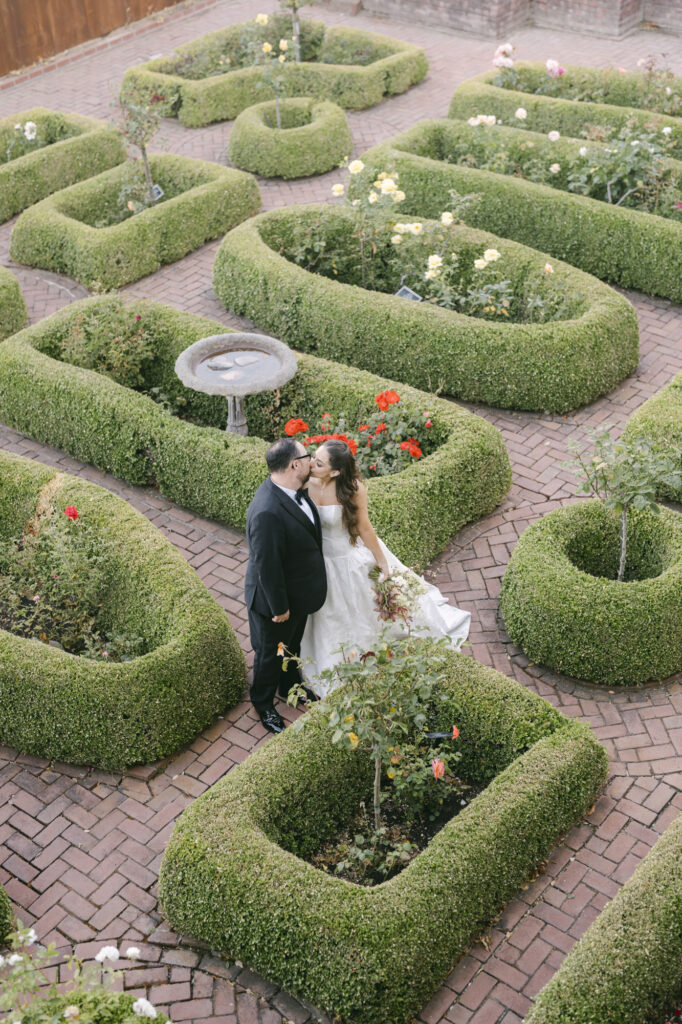 Aerial view of bride and groom standing in the formal knot garden at Kohl Mansion with geometric boxwood hedges and brick pathways