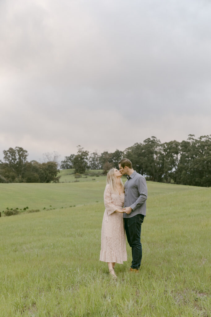 Couple kissing in a wide open green field at Arastradero Preserve Palo Alto during their Bay Area engagement photos