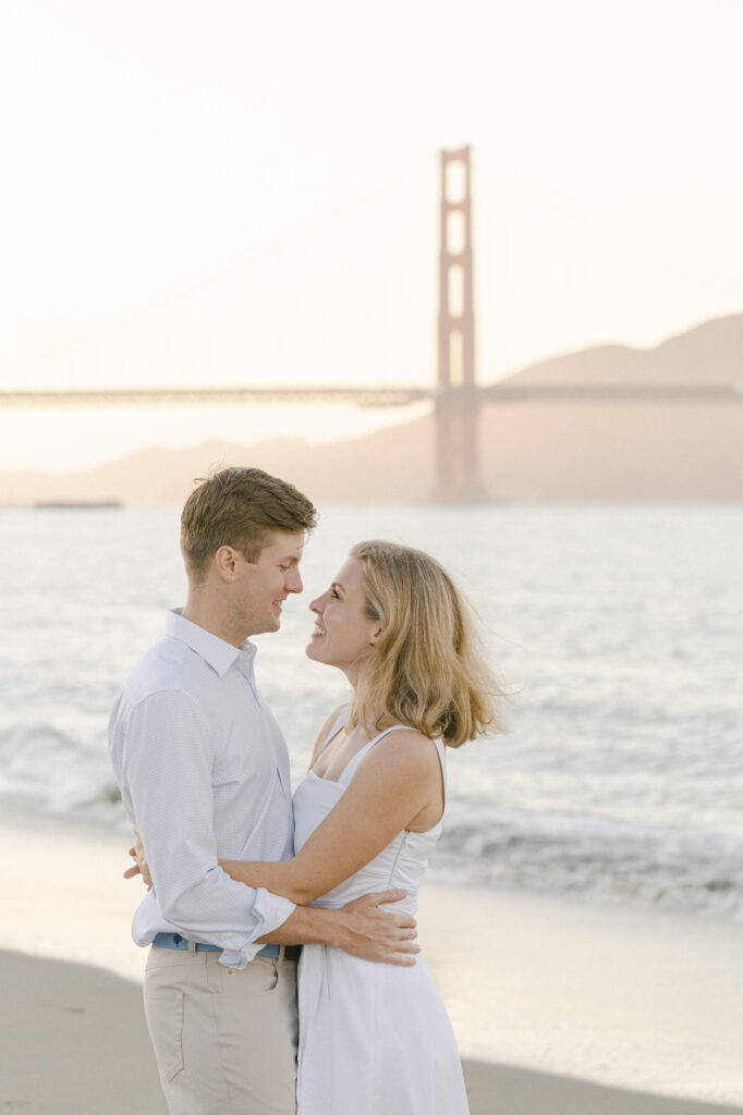Couple gazing at each other with the Golden Gate Bridge and Pacific Ocean behind them at Crissy Fields East Beach San Francisco