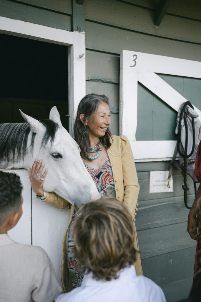 A wedding guest petting a white horse outside the green stable doors at Double H Ranch at Stonepine Estate in Carmel Valley