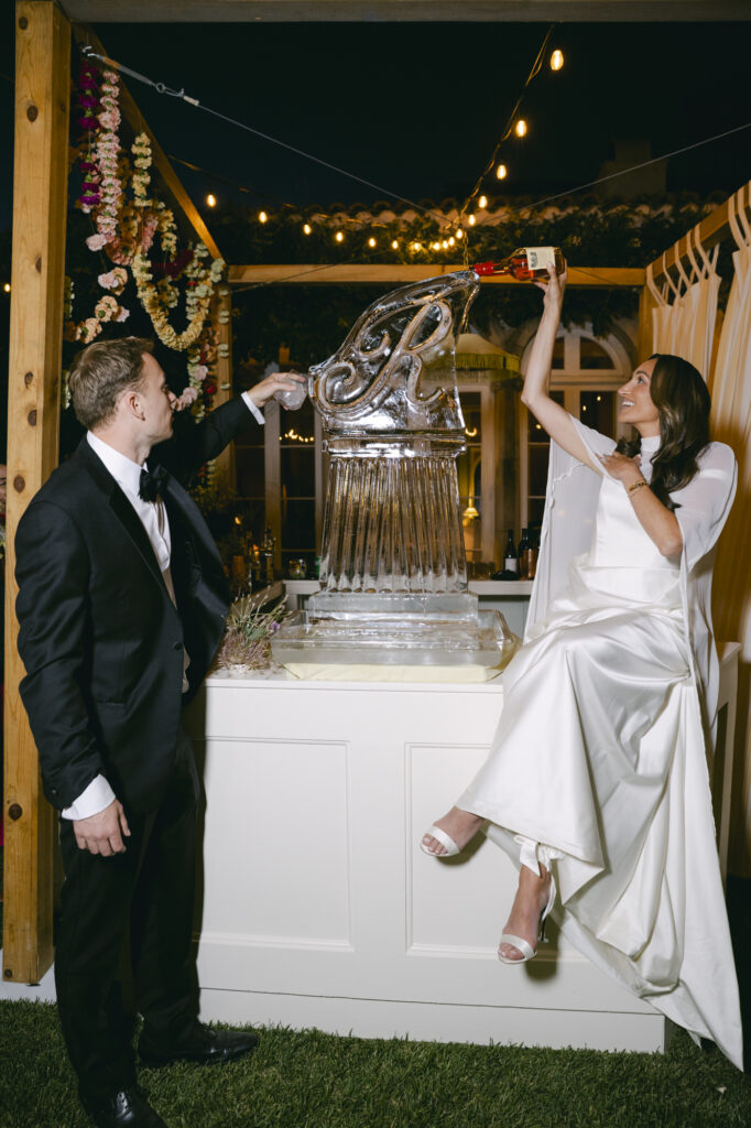 Bride and groom laughing together at a monogram ice luge inside the Blacksmith Bar at Stonepine Estate, string lights and floral installations glowing in the background