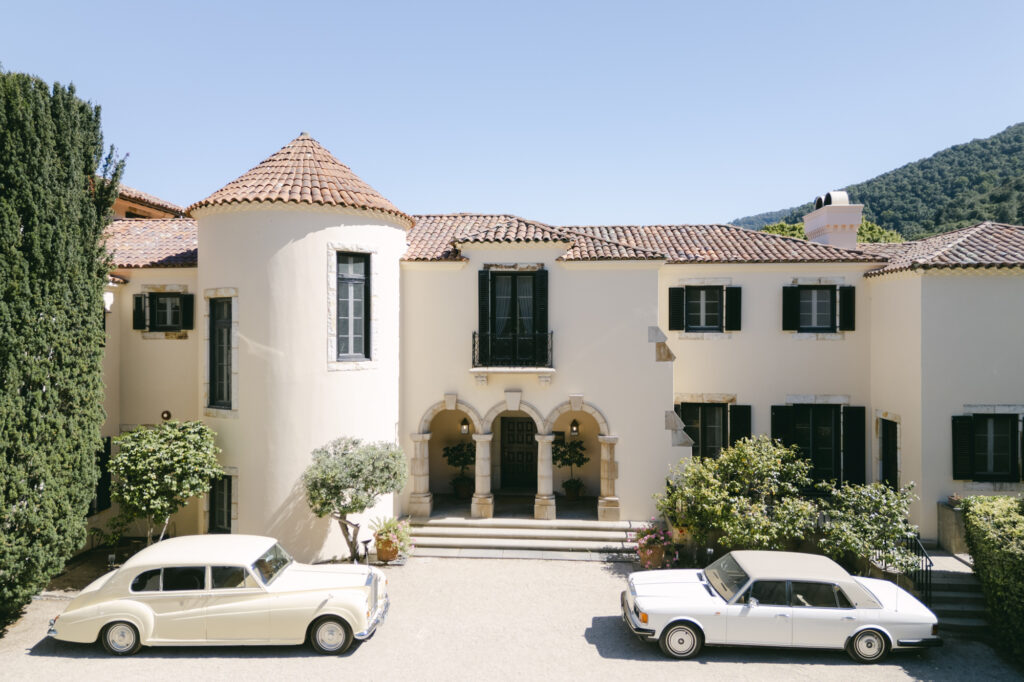 Exterior of Chateau Noel at Stonepine Estate in Carmel Valley, a white stucco Tuscan-style villa with a terracotta roof, arched entryway, and two vintage white cars parked in the courtyard