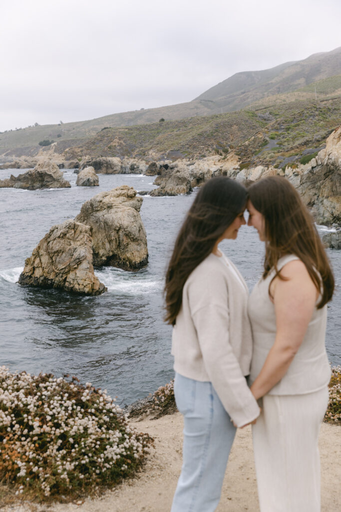 Newly engaged couple standing forehead to forehead on rocky coastline at Garrapata State Park