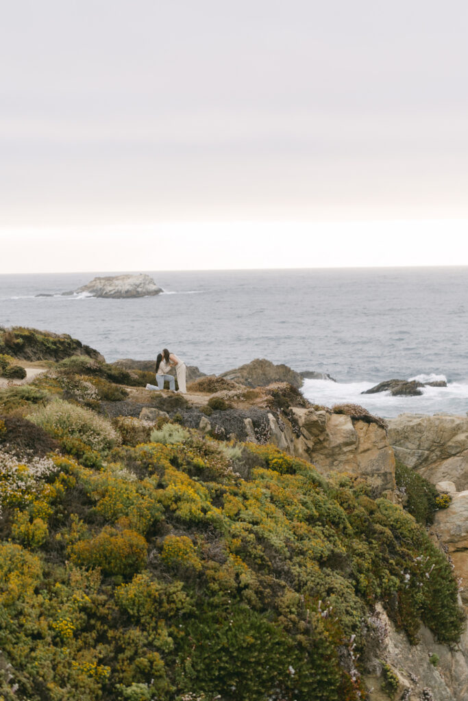 Wide shot of couple getting engaged on rocky cliffs overlooking the ocean at Garrapata State Park near Carmel