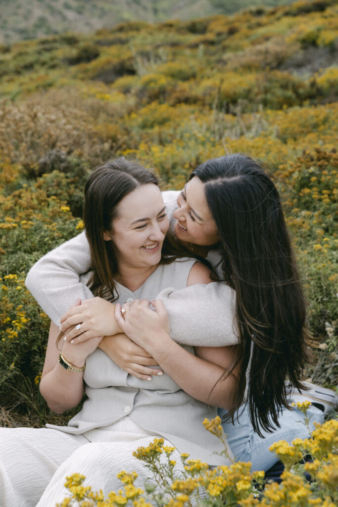 Engaged couple laughing and embracing in yellow wildflowers at Garrapata State Park in Carmel