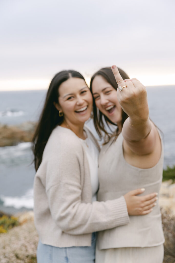 Newly engaged couple laughing and showing off engagement ring at Garrapata State Park in Carmel