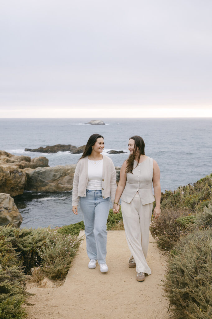Engaged couple holding hands and walking along coastal path at Garrapata State Park near Carmel